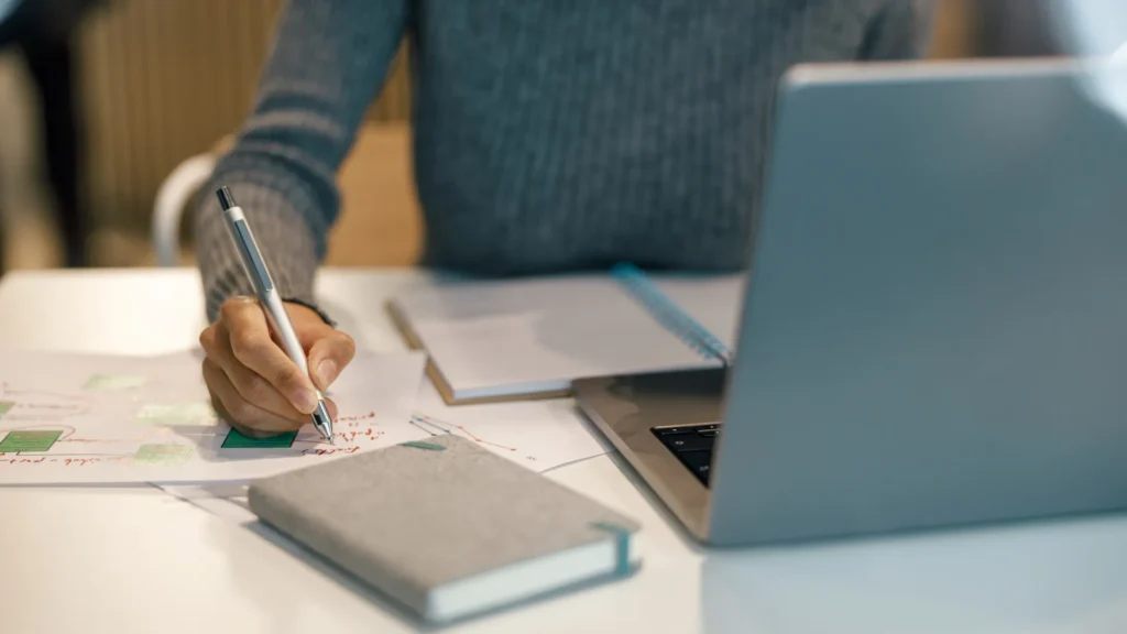 Person writing a marketing plan next to a laptop